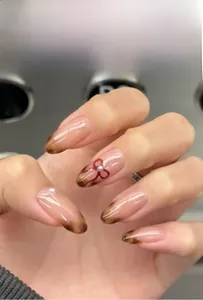 Detail of leopard print press-on nails with bow and pearl accents on brown cat-eye base