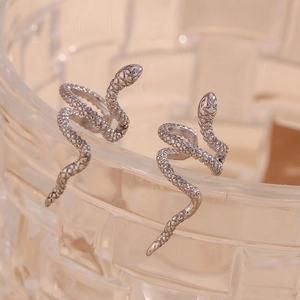Macro shot of silver snake-shaped earrings with realistic scale texture on glass rim