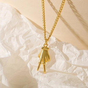Close-up of a 18k gold plated necklace with a hand gesture pendant on white paper