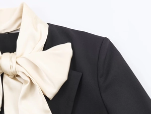 Close-up of contrast ivory satin bow detail on elegant black blazer lapel texture