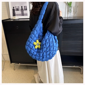 Blue quilted puff shoulder bag with a yellow flower charm on a model in a lifestyle setting