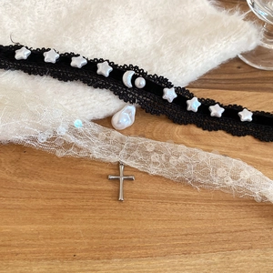 Détail de ras du cou en dentelle avec perle et collier croix à paillettes sur bois