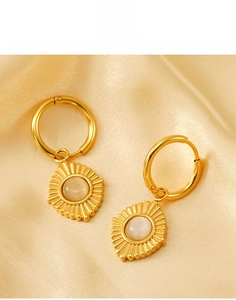 Détail de boucles d'oreilles en acier titane doré avec opale sur fond de soie douce