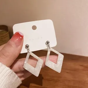 Close-up of white marble pattern resin rhombus geometric earrings held in hand