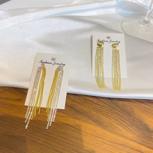 Detail of long gold tassel earrings with zircon pave and chain fringe on satin background
