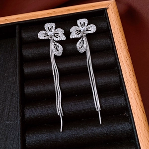 Detailed close-up of floral zircon earrings with long silver tassel on black velvet
