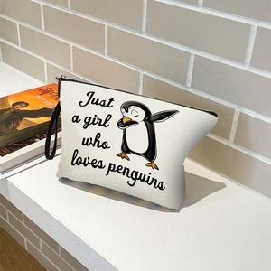 White canvas makeup bag featuring cartoon penguin print and black handle on wood surface