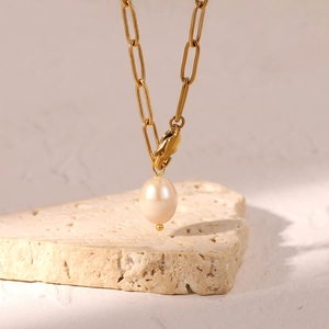 Gold paperclip chain necklace with a teardrop freshwater pearl pendant on a beige stone