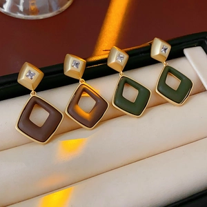 Close-up of geometric diamond earrings with brown and green resin in a jewelry box