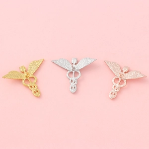 Medizinische Caduceus-Broschen in Gold, Silber und Roségold auf rosa Hintergrund