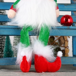 Detail of Christmas plush gnome with long legs and red shoes on a wooden bench