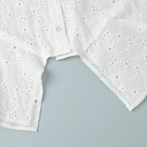 Detail of white eyelet embroidery on a loose summer dress with round button closure