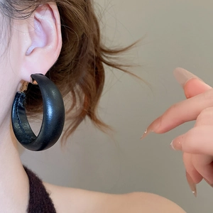 Macro detail of thick C-shaped black leather wrapped hoop earrings with gold metal clasp