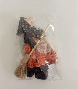 Detail of a cute Halloween witch doll with orange mesh skirt and a wooden broom in packaging