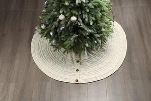Detail of cream cable knit Christmas tree skirt with decorative buttons on wood floor