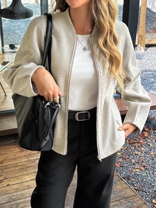 Giacca beige testurizzata con zip indossata in un caffè all'aperto con borsa nera