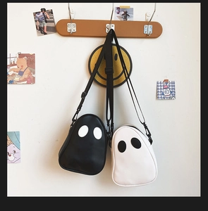 Cute black and white ghost-shaped PU leather crossbody bags hanging on wooden hooks