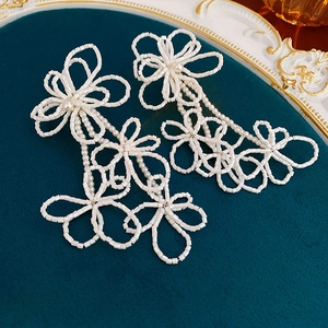 Detail of white beaded floral earrings on dark velvet background with luxury aesthetic