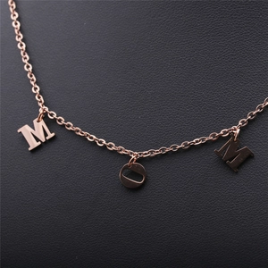 Close-up of rose gold stainless steel MOM letter necklace on black leather surface