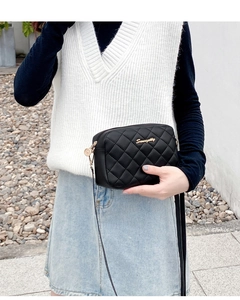 Detailed street style view of a black quilted crossbody bag with gold metal logo detail