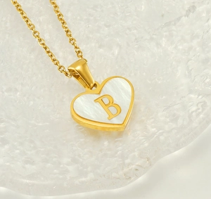 Macro detail of heart necklace with white shell inlay and golden initial B pendant