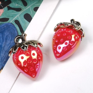 Macro shot of red strawberry pendant with glossy metallic gold leaves on white surface