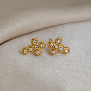 Macro shot of 18K gold plated cross earrings with sparkling cubic zirconia on beige fabric