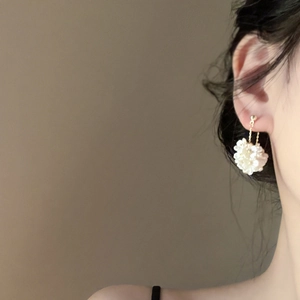 Elegant floral pearl earring with gold chain shown on a model against a warm grey background