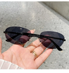 Detail view of oval rimless sunglasses with black lenses and slim metal temples held by hand