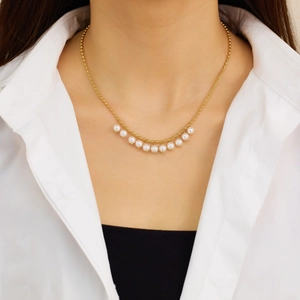 Elegant gold beaded necklace with eleven white pearls on a model wearing a white shirt