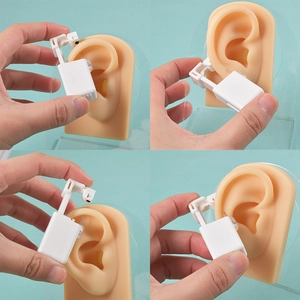 Manual ear piercing gun tool demonstrated on silicone ear model with stud earrings