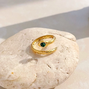 Adjustable gold snake ring with green gemstone on natural stone background