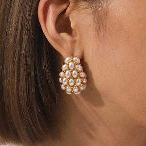 Macro view of gold teardrop earrings featuring clustered white pearls on model