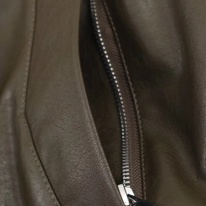 Detail von Metallreißverschluss und verstärkten Nähten an einer grünen Pilotenjacke
