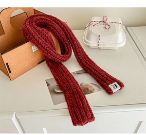 Close-up of a red wool knit scarf with a textured weave and a small white brand label