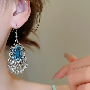 Primo piano di orecchini boho in argento con pietre blu e frange di nappe su una modella