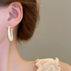 Close-up of model wearing cream-colored C-shaped oval hoop earrings with a matte finish