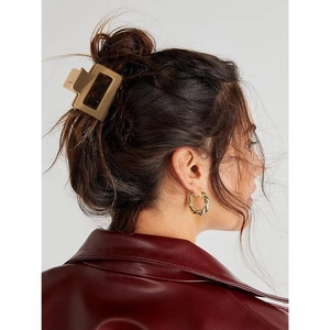 Detail view of square matte hair claw and golden twist hoop earrings on a model
