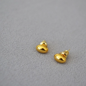 Detailed view of gold bean earrings with a polished mirror finish on soft grey fabric