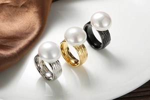 Detailed view of three textured stainless steel rings with large pearls in silver gold and black
