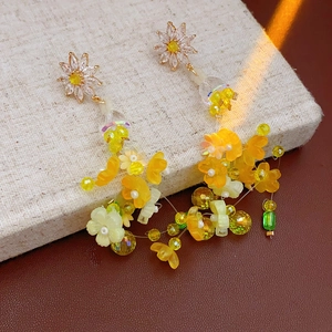 Détail de boucles d'oreilles fleurs jaunes à pompons et cristaux sur support lin