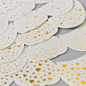 Detailed view of gold foil freckle stickers with heart and star patterns on white backing