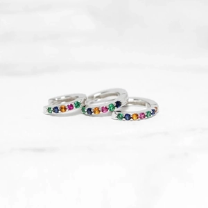 Close-up of three silver hoop earrings with multicolored zircon stones on marble