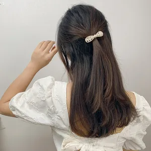 Detail of elegant gold bow hair clip with white pearls worn on long curly hair
