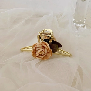 Detail of elegant gold metal hair claw clip with a beige fabric rose on soft white tulle