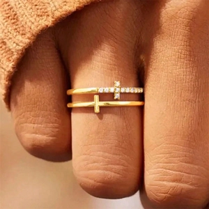 Double-layered gold cross ring with small crystals worn on a finger as a stylish accessory