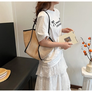 Spacious beige woven straw tote bag with black handles shown on model for summer style