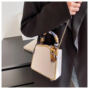 Detail of beige structured box bag featuring a silk scarf handle and gold chain strap
