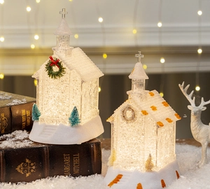 Close-up of two glowing crystal church ornaments with warm LED lights and faux snow
