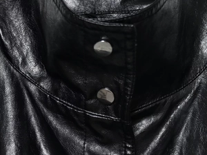 Detail of black leather bomber jacket featuring silver metal snap buttons and smooth texture